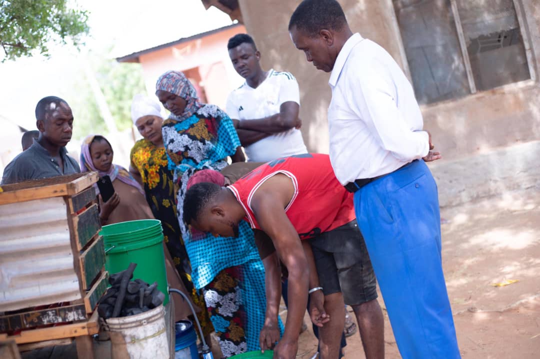 People gathered in a village learning how to use water filtration buckets, demonstrating practical clean water solutions outdoors.